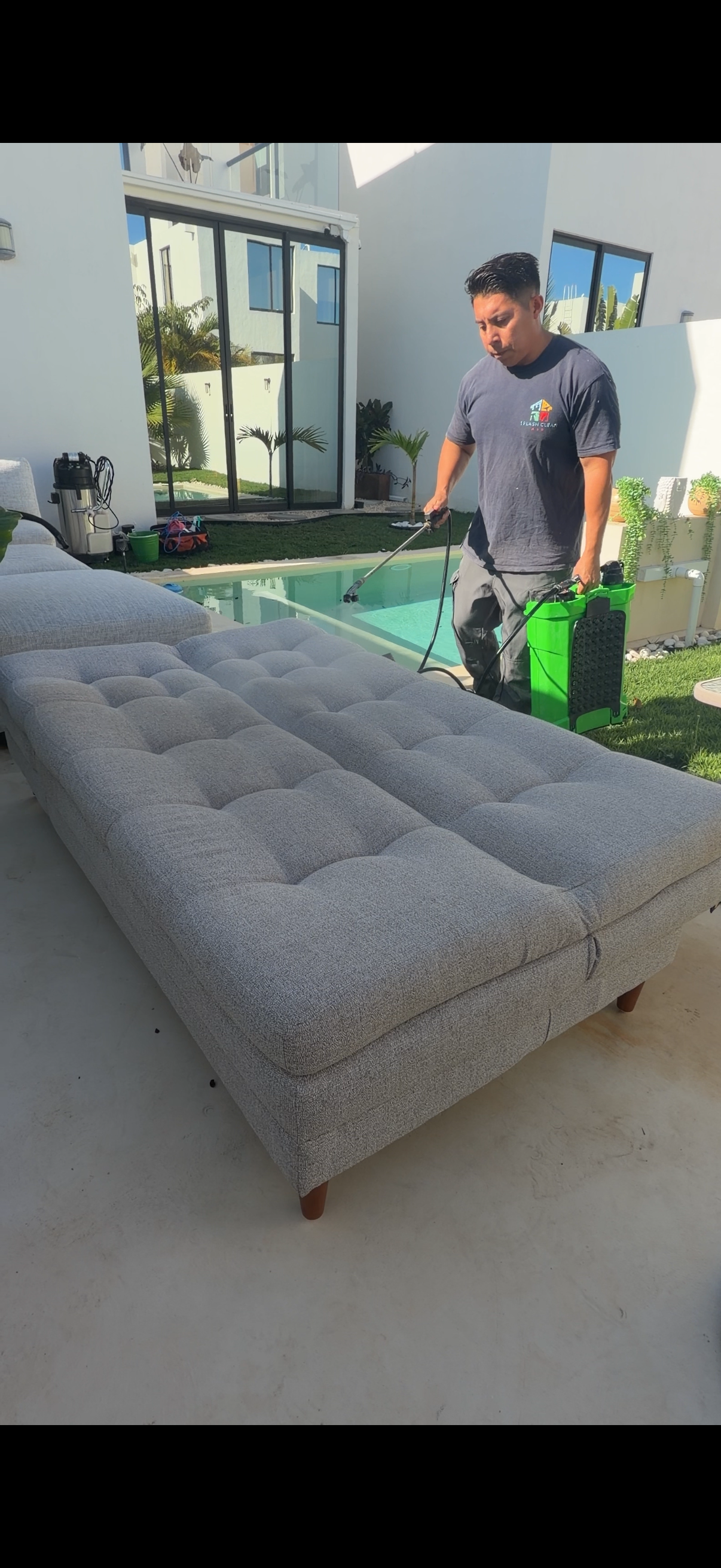 Persona aplicando limpieza a un sofá cama gris claro en un patio.