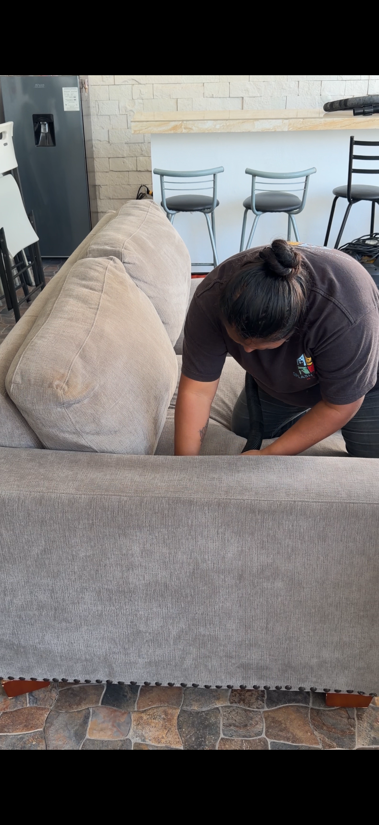 Persona limpiando el respaldo de un sofá beige en un interior.